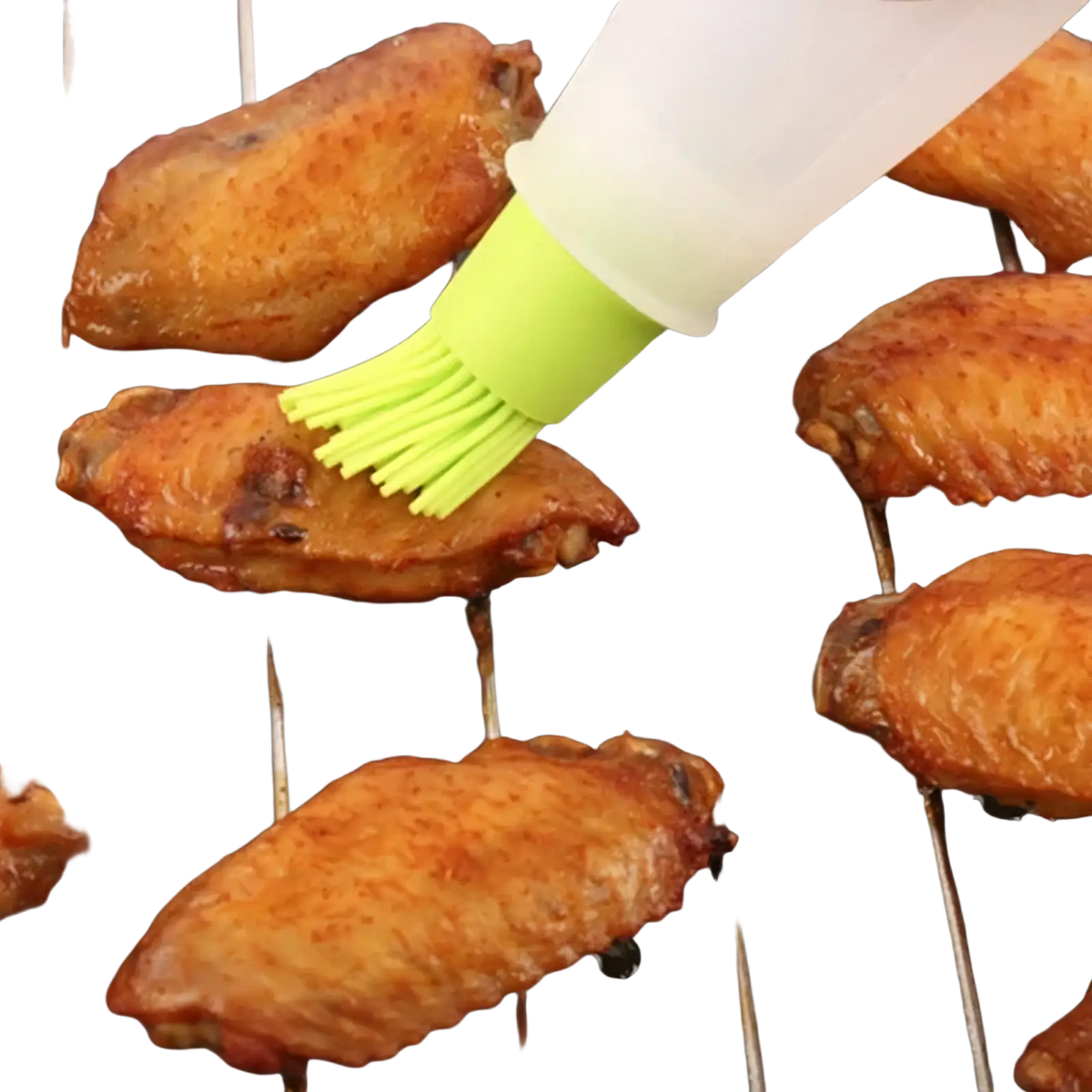 A translucent white silicone oil dispenser brush with bright lime green bristles applying sauce to grilled chicken wings