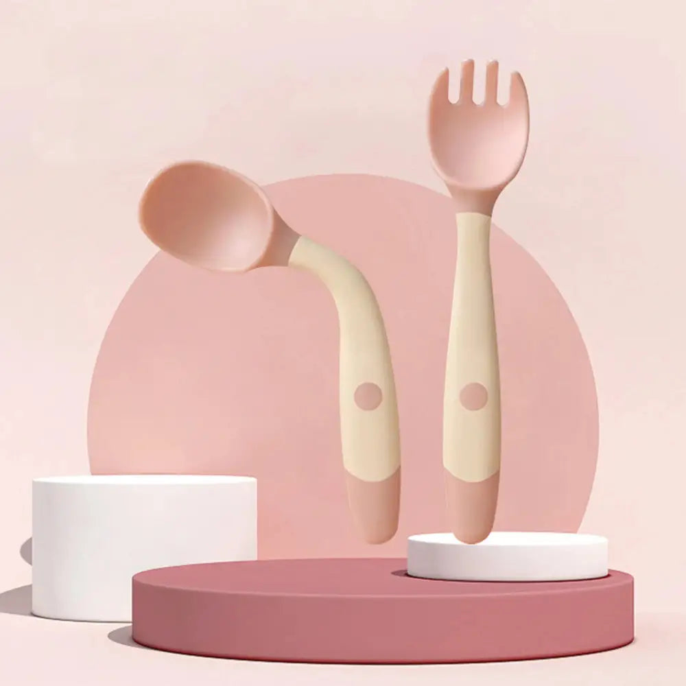 Soft silicone baby spoon and fork self feeding set in pastel pink and cream with rounded handles and small circular detail