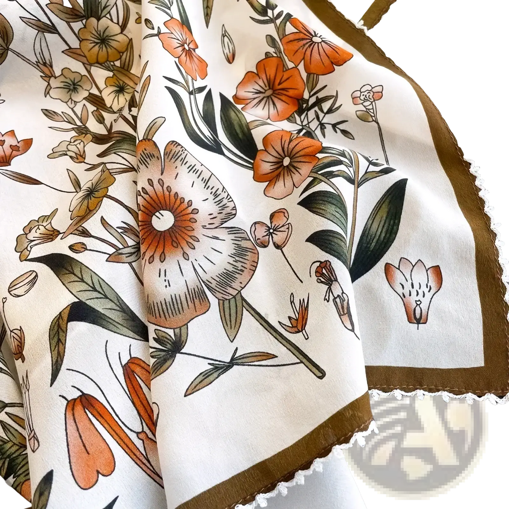 A cream-colored silk floral square scarf with orange peach and green botanical print brown border and white lace trim