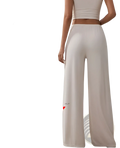 Beige silk wide leg yoga pants with silver silicone mlp logo on the lower leg featuring a relaxed fit