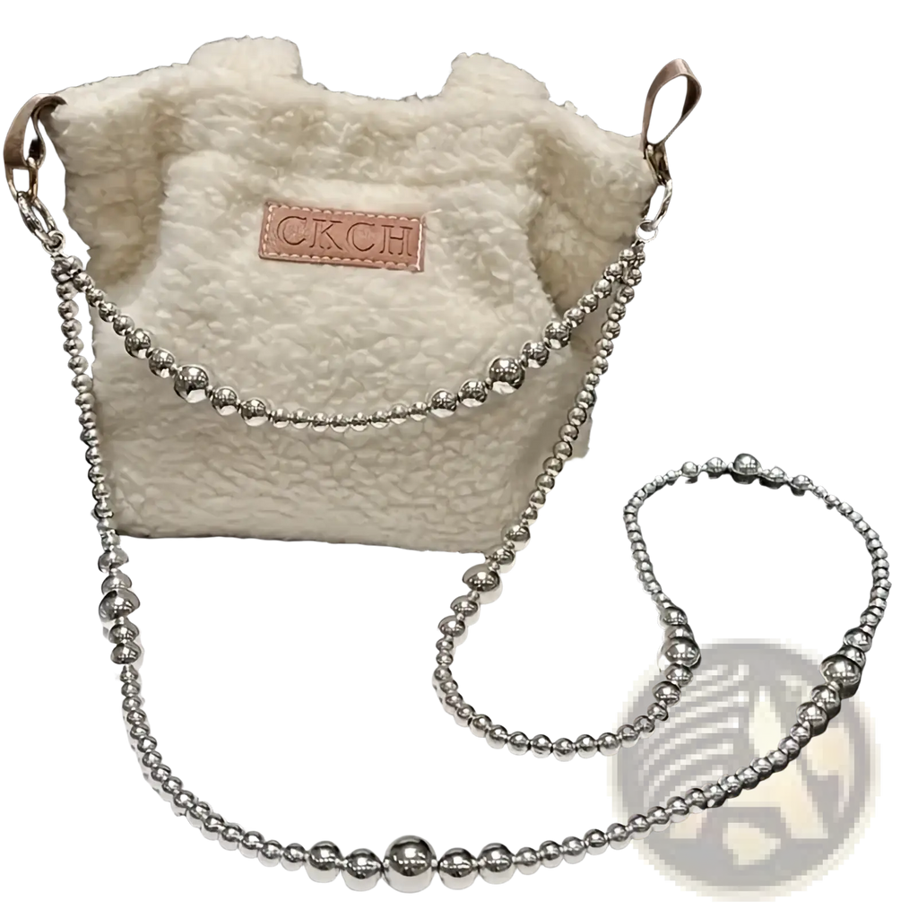 A fluffy white shearling bucket bag with a silver beaded chain strap and brown leather ckch patch