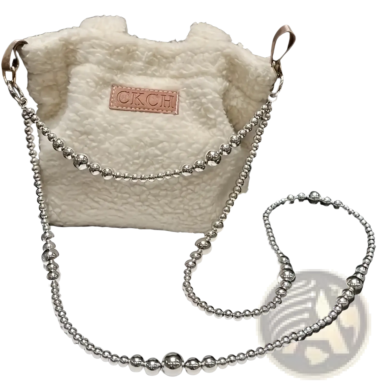 A fluffy white shearling bucket bag with a silver beaded chain strap and brown leather ckch patch