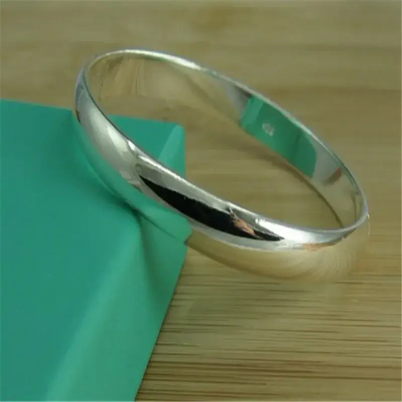 A sleek silver bracelet 925 sterling open bangle for women rests on a teal surface in brazaletes pulseras mujer style