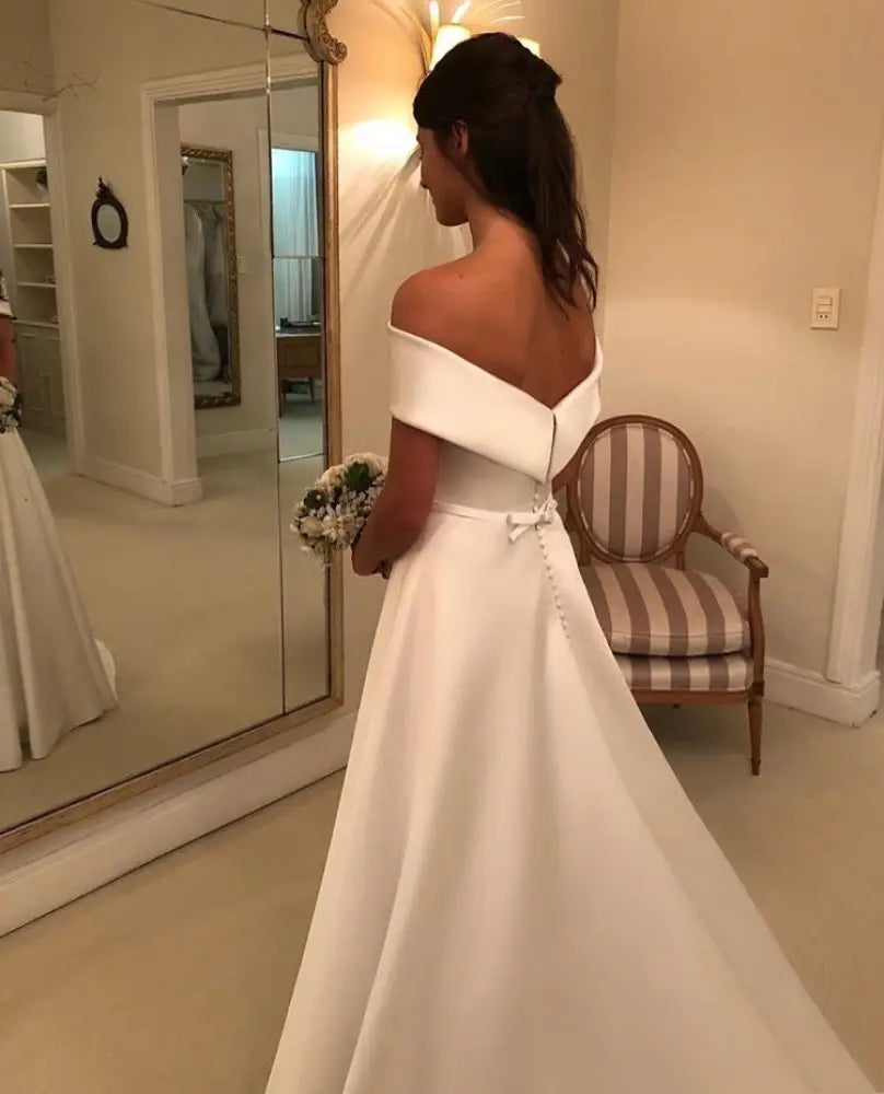A sleek off the shoulder white satin a line wedding gown with fitted bodice and flowing sweep train