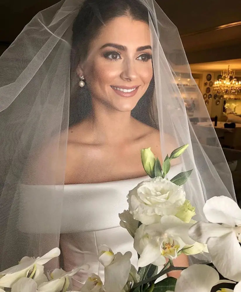 Off the shoulder satin a line wedding gown with sweep train featuring a delicate sheer white veil over the bride’s shoulders