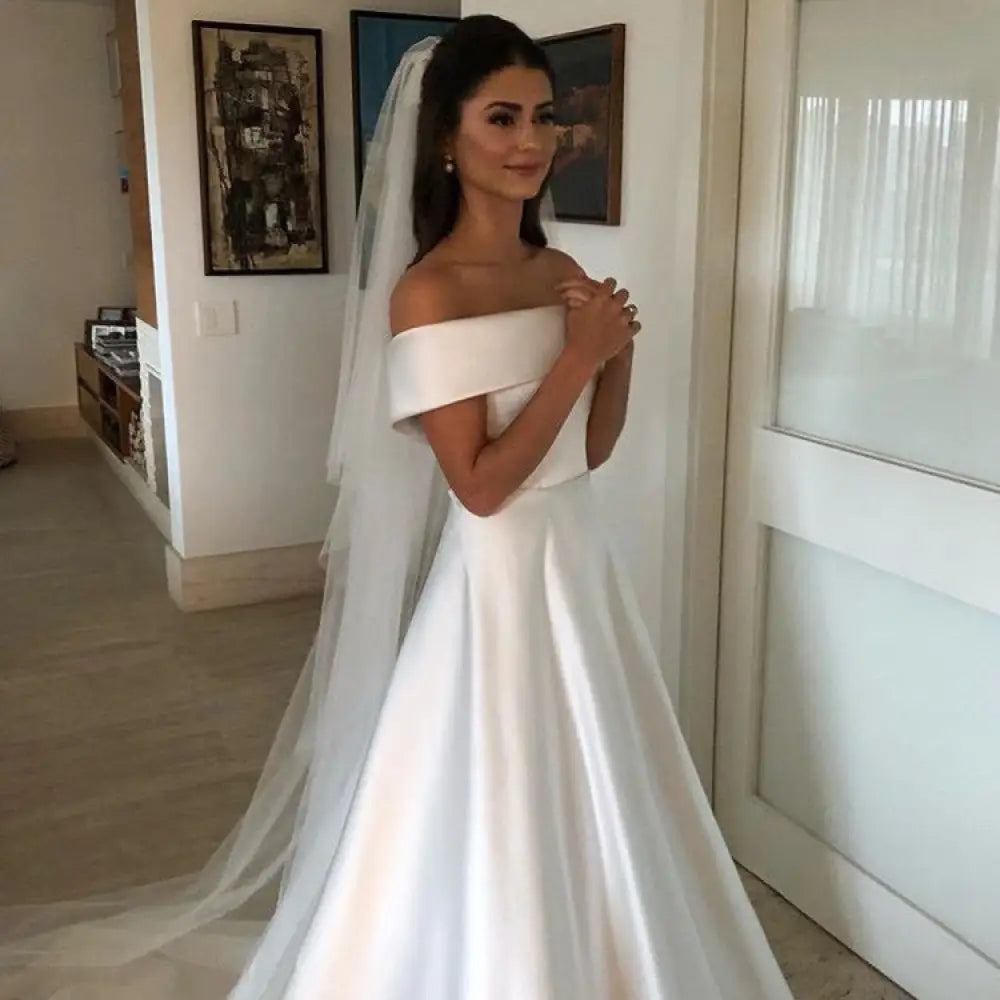White satin off the shoulder a line wedding gown with sweep train and flowing veil shown from the back side