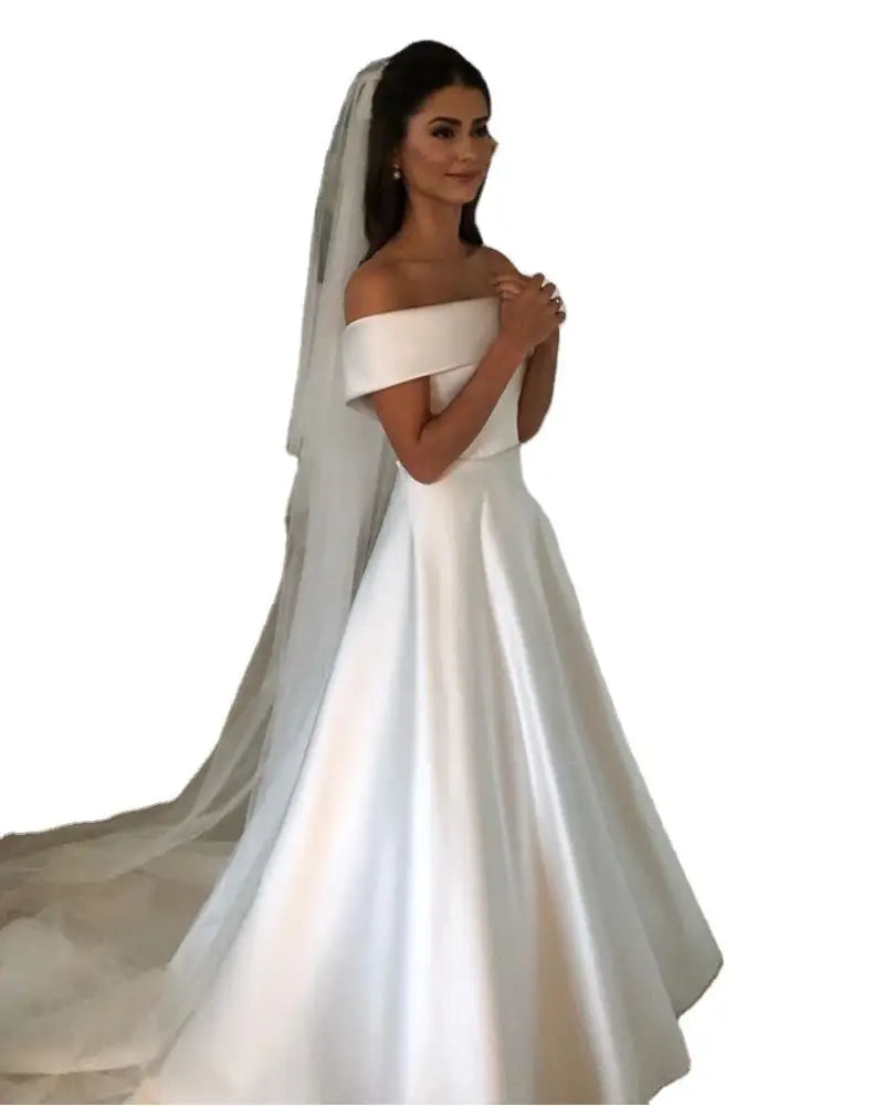 Off the shoulder white satin a line wedding gown with fitted bodice voluminous skirt and attached sheer veil