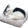 A plush black and white simulated sleeping cat toy with sound curled up on a textured gray cushion with a pink nose