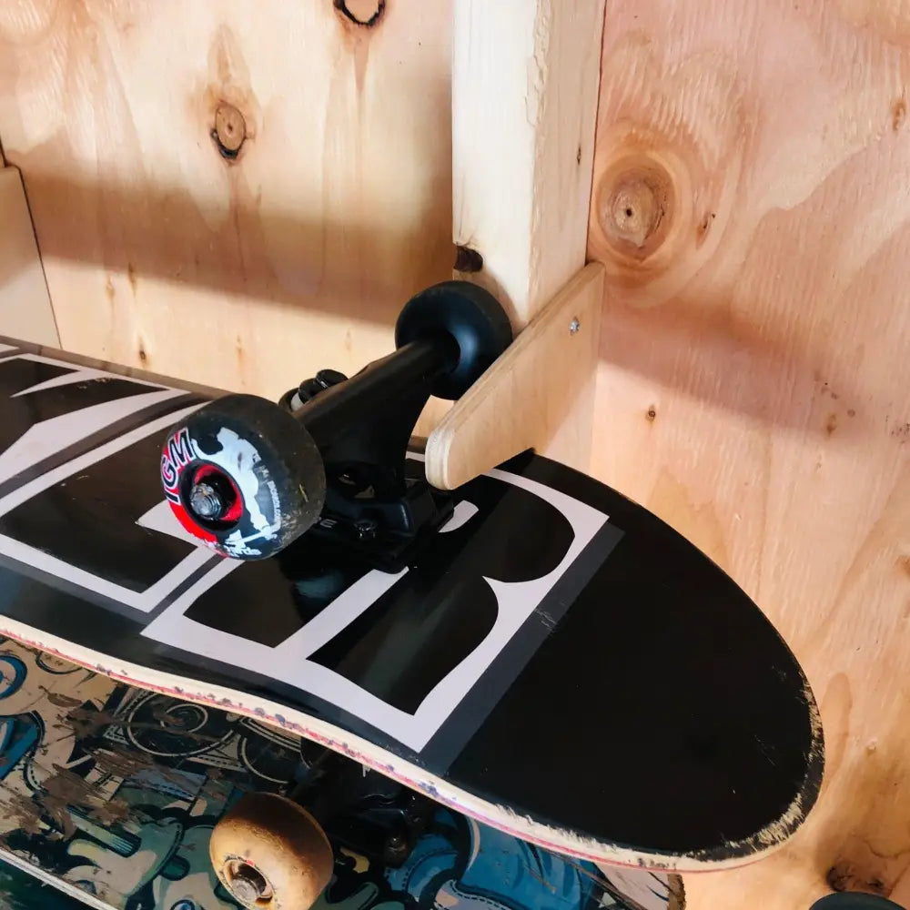 Vertical wooden skateboard wall mount storage rack holding a black skateboard with white graphics and red and white wheels