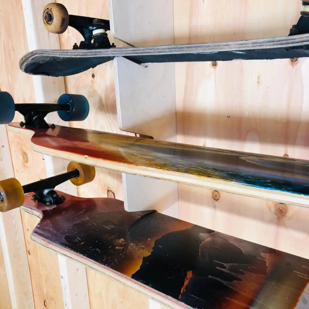 Three longboard skateboards with colorful painted decks and yellow wheels mounted vertically on a wooden wall rack storage unit