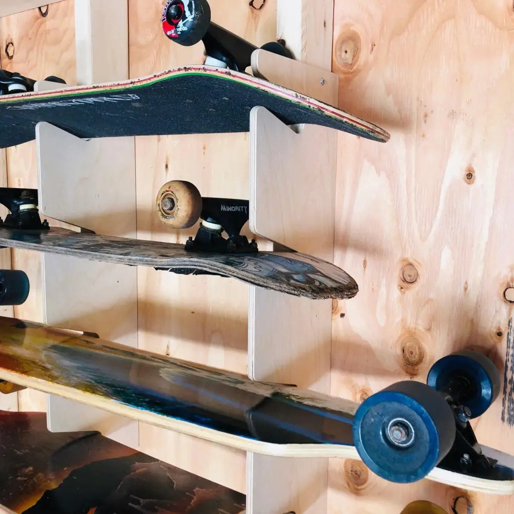 Wooden vertical skateboard wall mount storage rack holding three skateboards with varied deck designs and colored wheels