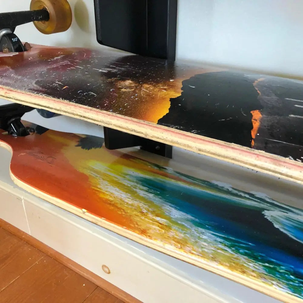 Multi deck vertical skateboard and snowboard wall rack holding two longboards with vibrant abstract fiery and ocean wave graphics