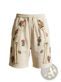Cream-colored polyester sweat shorts featuring embroidered floral and textured bone designs along the sides