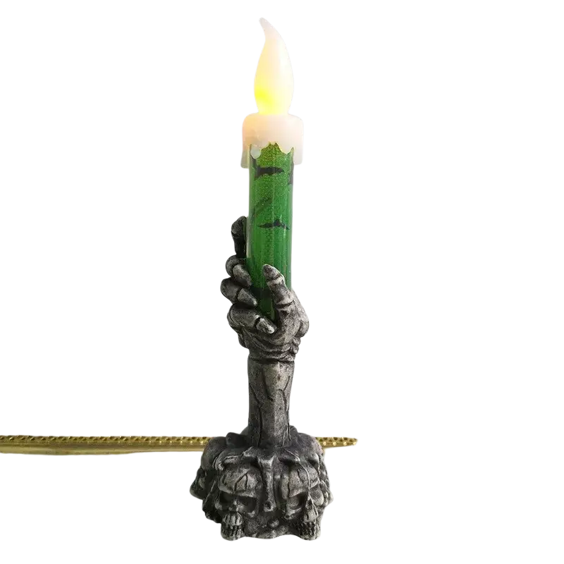 A green led candle with a glowing flame held by a silver skeleton hand base decorated with skulls for a happy halloween party