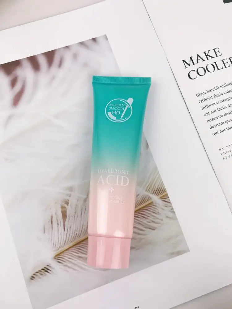 A gradient teal to pink tube of hyaluronic acid hydrating skincare with white circular logo and gold lettering