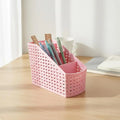 Slanted woven plastic desk organizer in pink with a lattice design and multiple compartments for pens and supplies