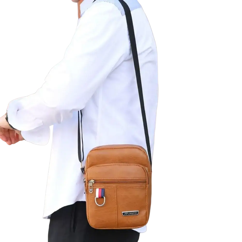 Tan leather sling bag messenger with black strap and flag emblem on zipper pull for casual use