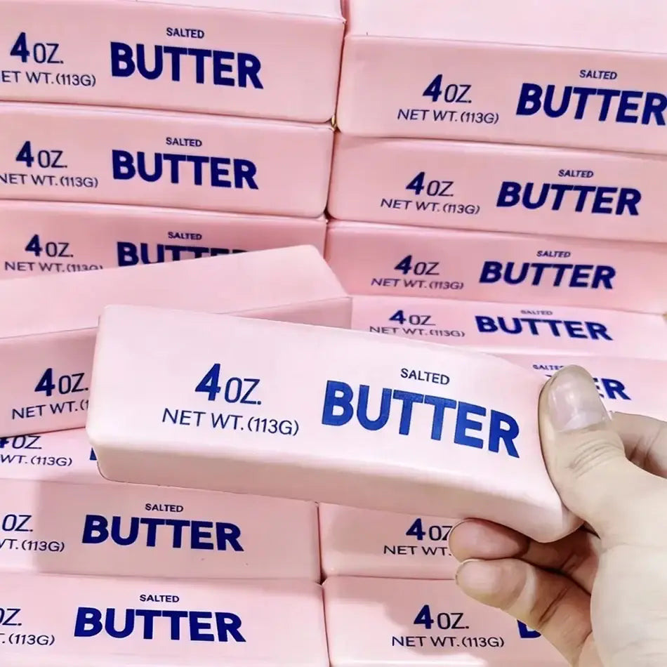 A hand holds a pink slow rising squishy butter squeeze toy shaped like a 4 oz salted butter package for stress relief