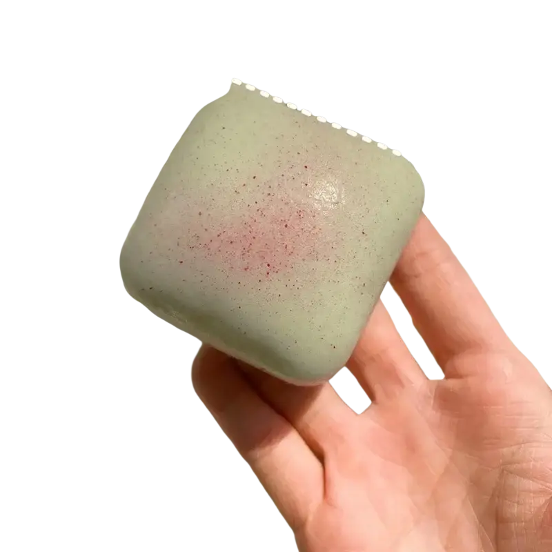 Slow rising squishy mini toast fidget toy in pale green speckled square soap bar with subtle pinkish hue on surface