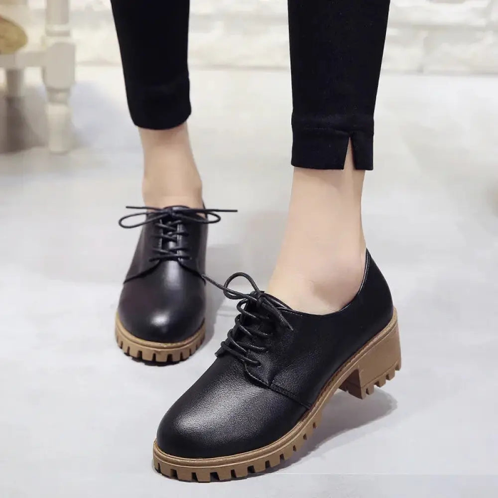 Women’s black leather lace up oxford shoes with chunky tan rubber sole shown from the back side