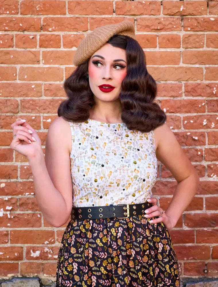 Woman wearing snailing along vintage 1950s floral twofer dress with black belt and beige beret in front view
