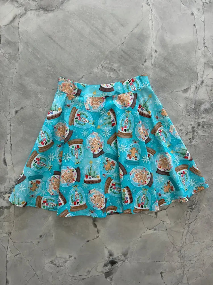 A turquoise cotton skater skirt with pleats featuring a festive gingerbread house and snow globe pattern