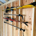 Durable wall mounted snow and water ski storage rack holding yellow and black skis with bindings on wooden wall rack