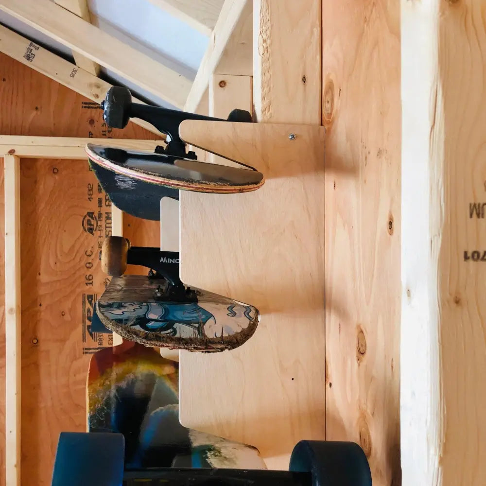 Two skateboards hang vertically on a birch plywood stud mounted snowboard and skateboard rack with a blue and white deck