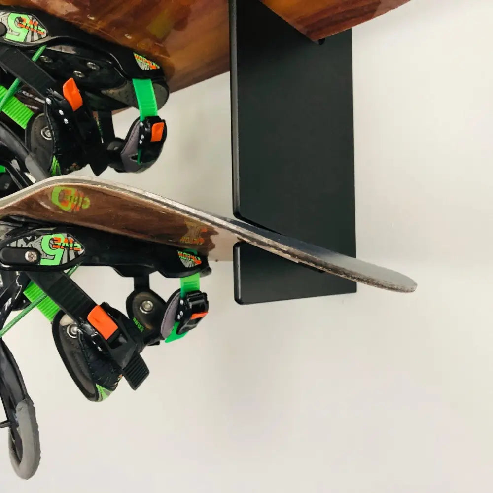 Handcrafted minimalist snowboard wall mount display rack holding a brown snowboard with green and black bindings and orange dials