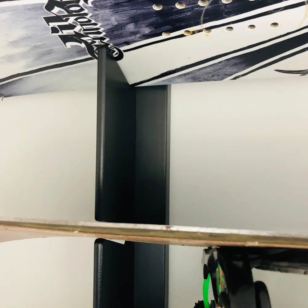 Black metal minimalist handcrafted snowboard wall mount rack holding a white and navy blue surfboard with black graphics