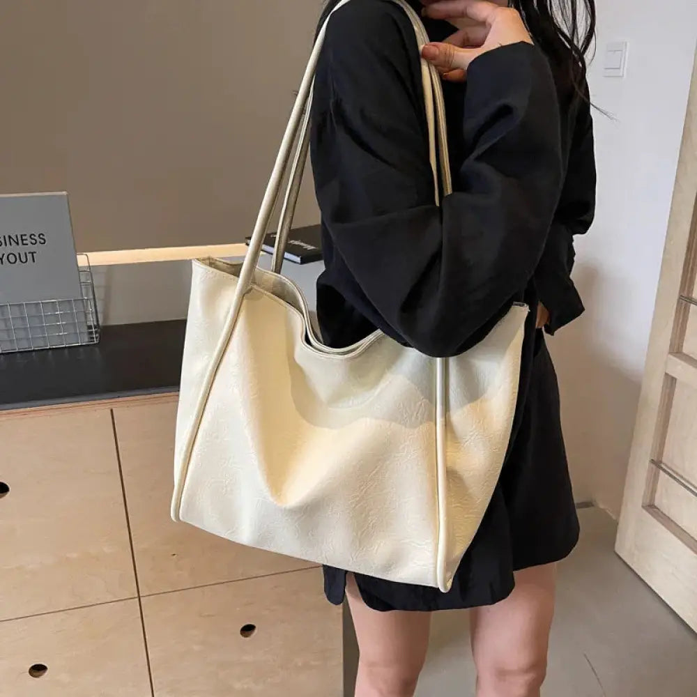 Cream-colored large faux leather minimalist commuter tote bag with long matching handles and soft textured fabric finish