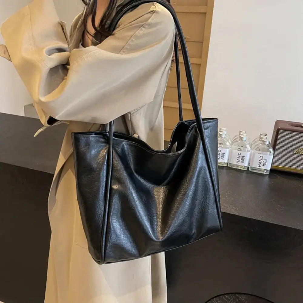 Black faux leather large minimalist commuter tote bag with long shoulder strap and sleek design