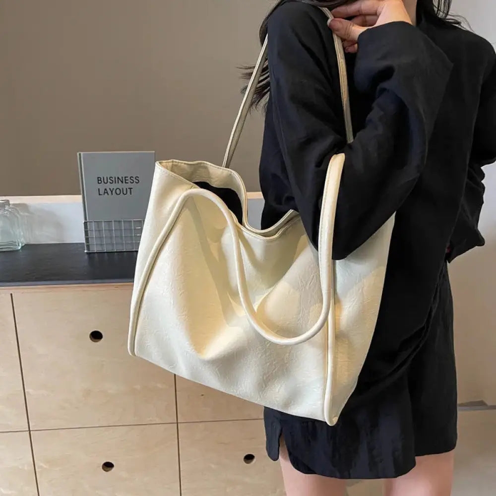 Cream-colored large minimalist commuter tote bag made of faux leather with soft slouchy canvas and matching handles