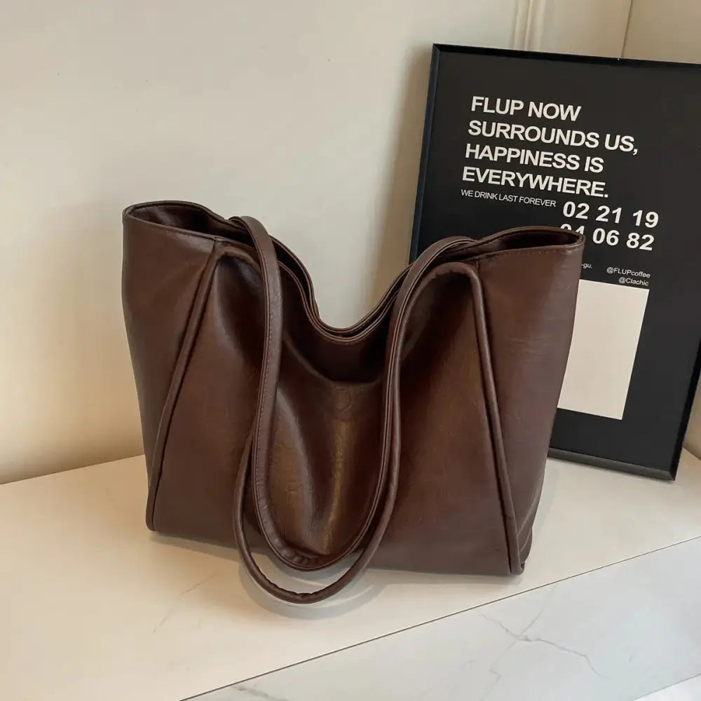 A sleek brown large faux leather minimalist commuter tote bag with soft slouchy folds and sturdy handles