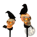 Solar skull and crow garden light featuring white skull-shaped solar lights with glowing orange interiors and black crows on stakes