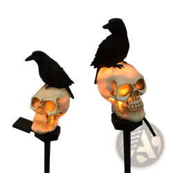 Solar skull and crow garden light featuring white skull-shaped solar lights with glowing orange interiors and black crows on stakes