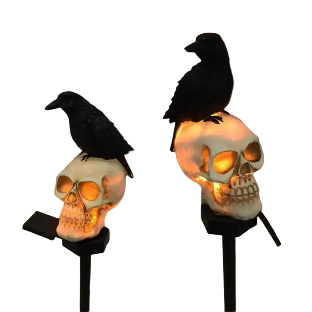 Two illuminated white solar skull garden stakes topped with black crow figurines and glowing orange eye sockets