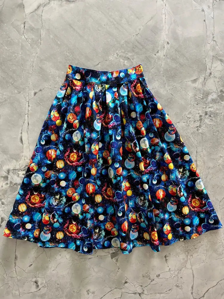 A flared cotton skirt with vibrant cosmic print of colorful planets and stars on dark blue fabric with pockets