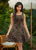 A sleeveless dark brown skater dress in fabric with colorful cityscape print featuring buildings and street elements