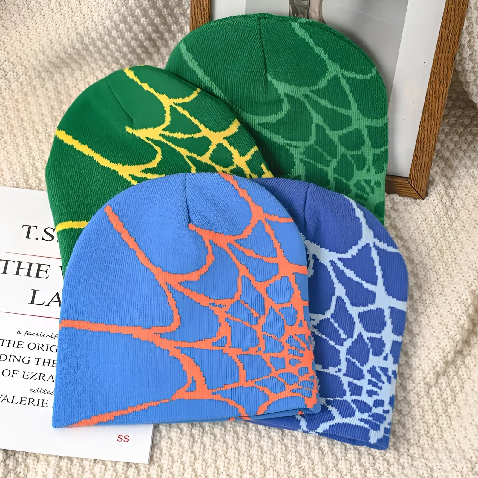 Three knitted spiderweb knit beanies in green, blue, and light blue with contrasting bold spiderweb patterns for winter wear