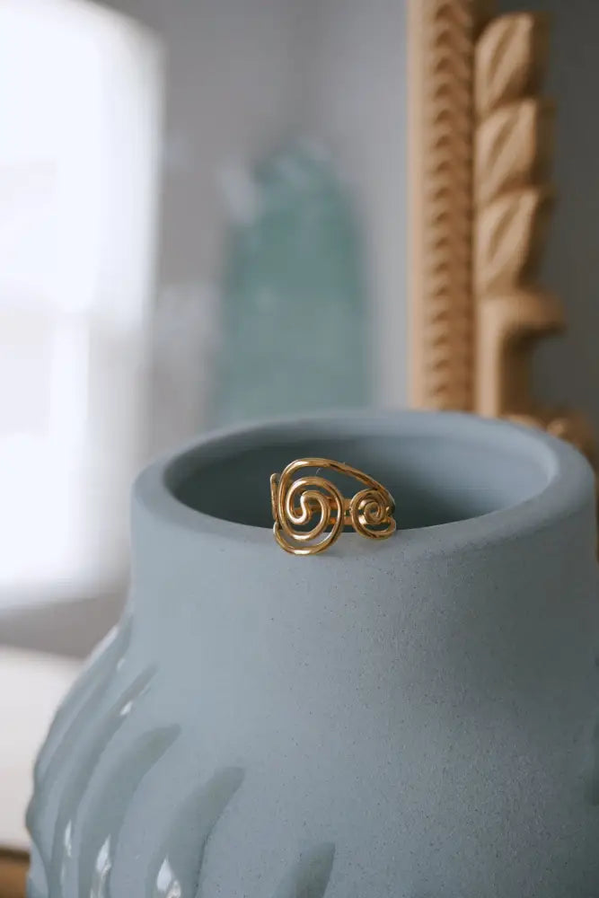 An adjustable gold spiral toe ring with gemstones displayed inside a light blue ceramic vase