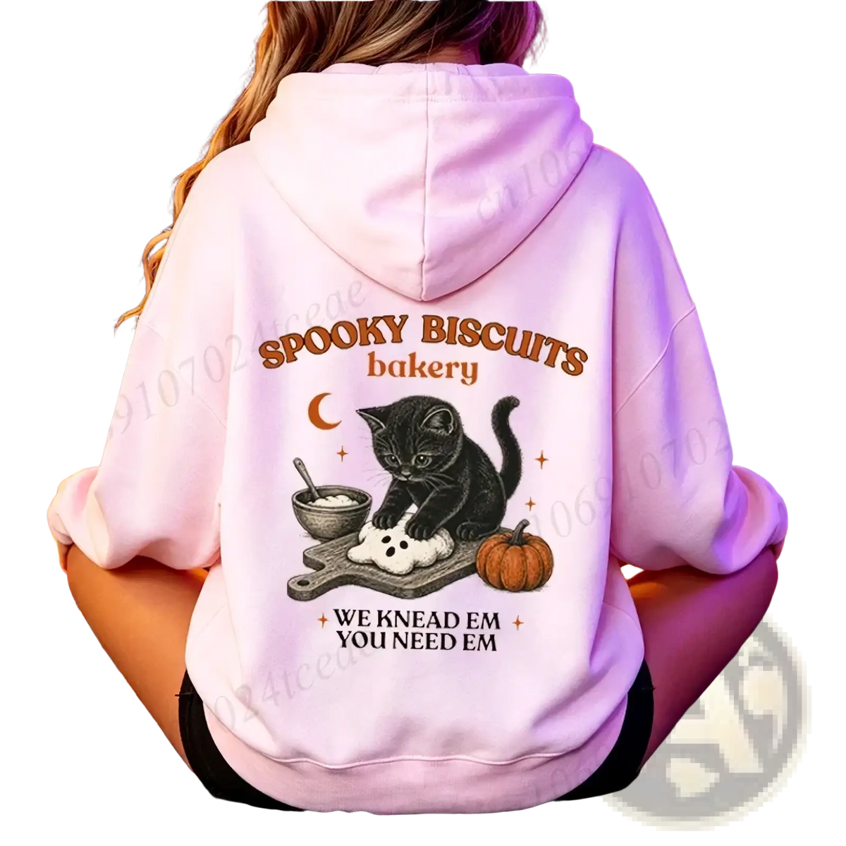 A soft pink hoodie featuring a halloween graphic of a black cat kneading dough with spooky biscuits bakery text