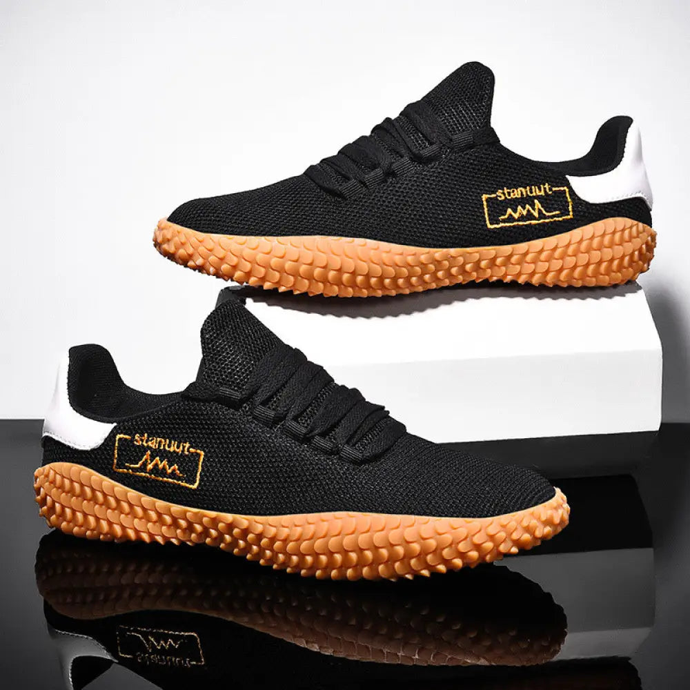 Black men’s breathable flying woven mesh sneakers with tan textured rubber sole and white heel accents shown from back