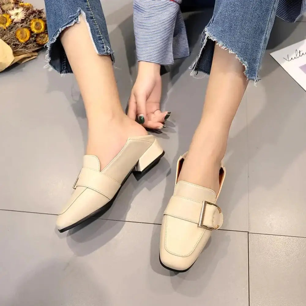 Cream-colored leather square toe buckle mules with a small block heel and decorative strap across the vamp