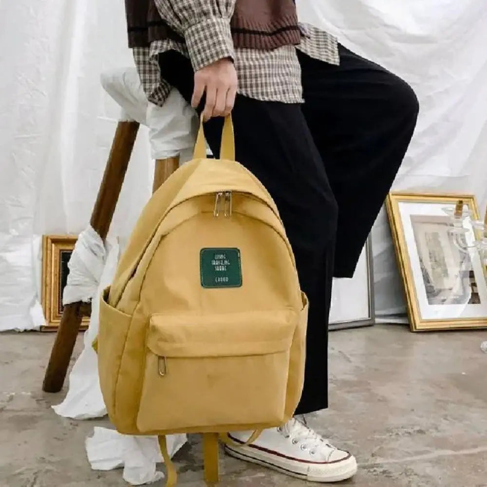 A mustard yellow canvas womens korean corduroy pastel school and travel backpack with a green patch and gold zippers