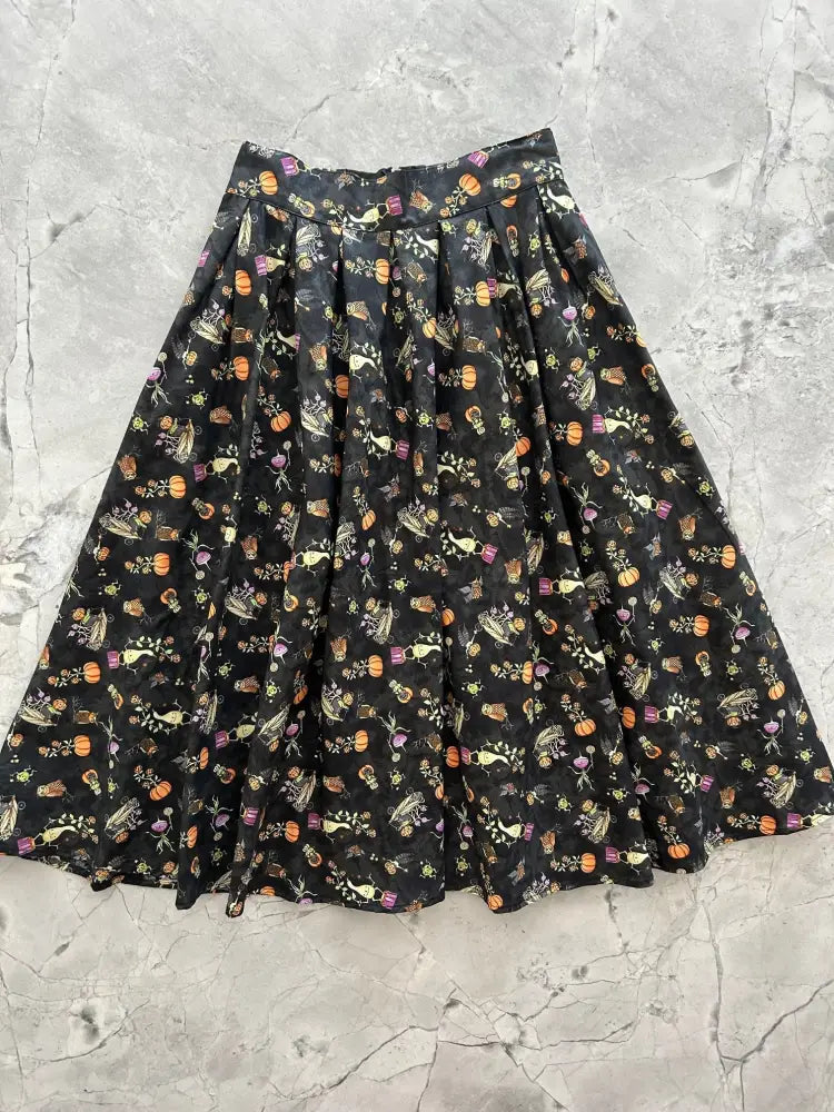 Black pleated skirt with pockets featuring a festive halloween pattern of orange pumpkins and pastel skulls