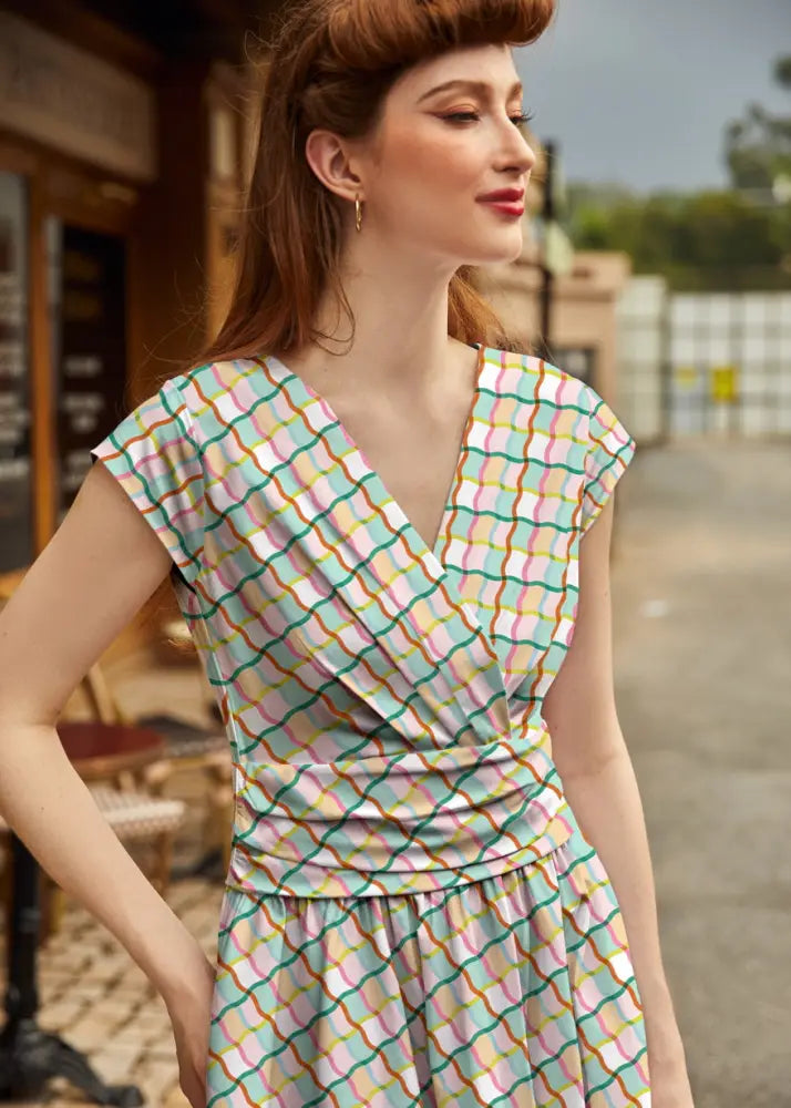 A woman wearing a squiggly greta vintage cotton wrap dress with pockets in pastel geometric grid mint and pink tones