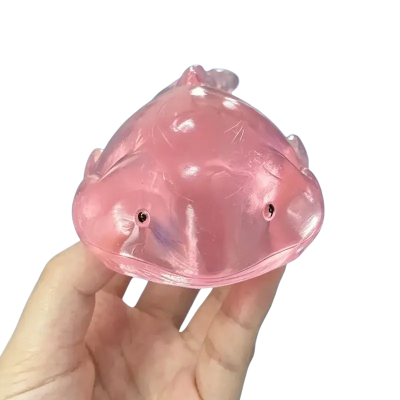 Translucent pink axolotl-shaped squishy whale fidget toy stress ball with small black eyes and glossy finish