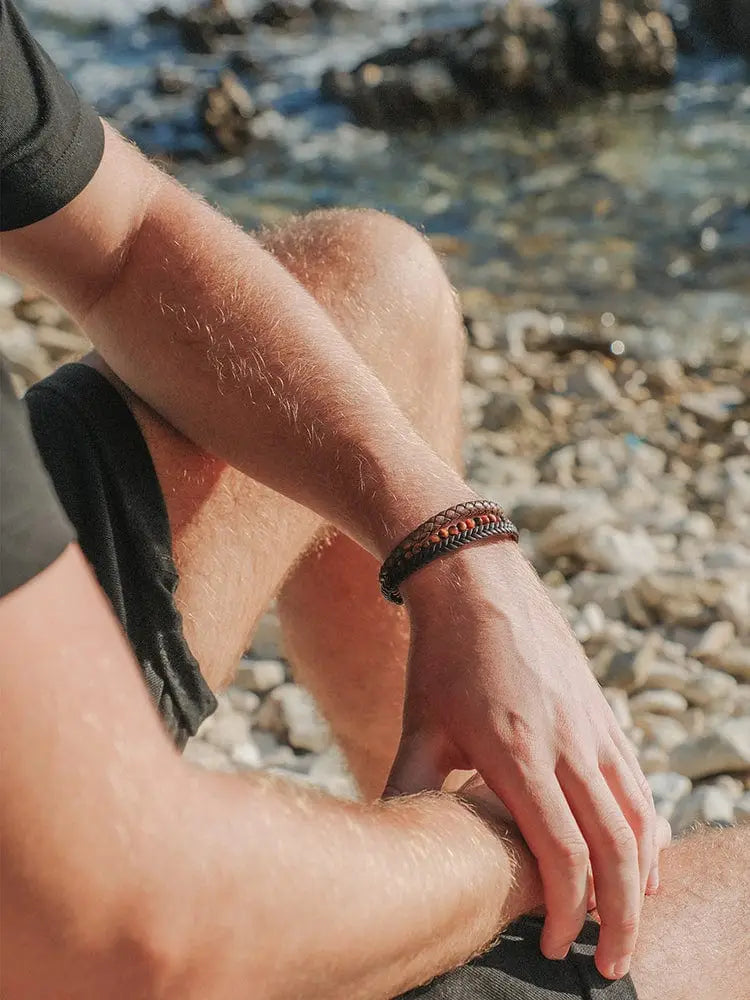 Stacked tiger eye and braided brown leather bracelet featuring a dark brown and black woven pattern on a mans wrist