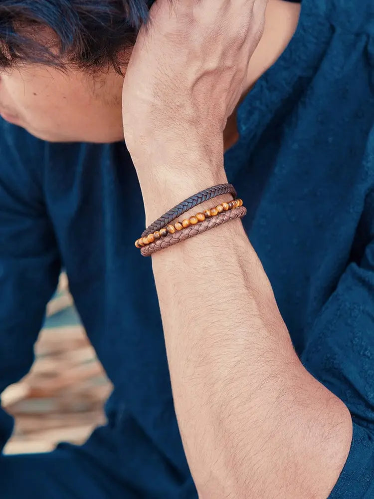 A set of three stacked braided leather bracelets in dark brown and tan with small golden beads for stylish wear